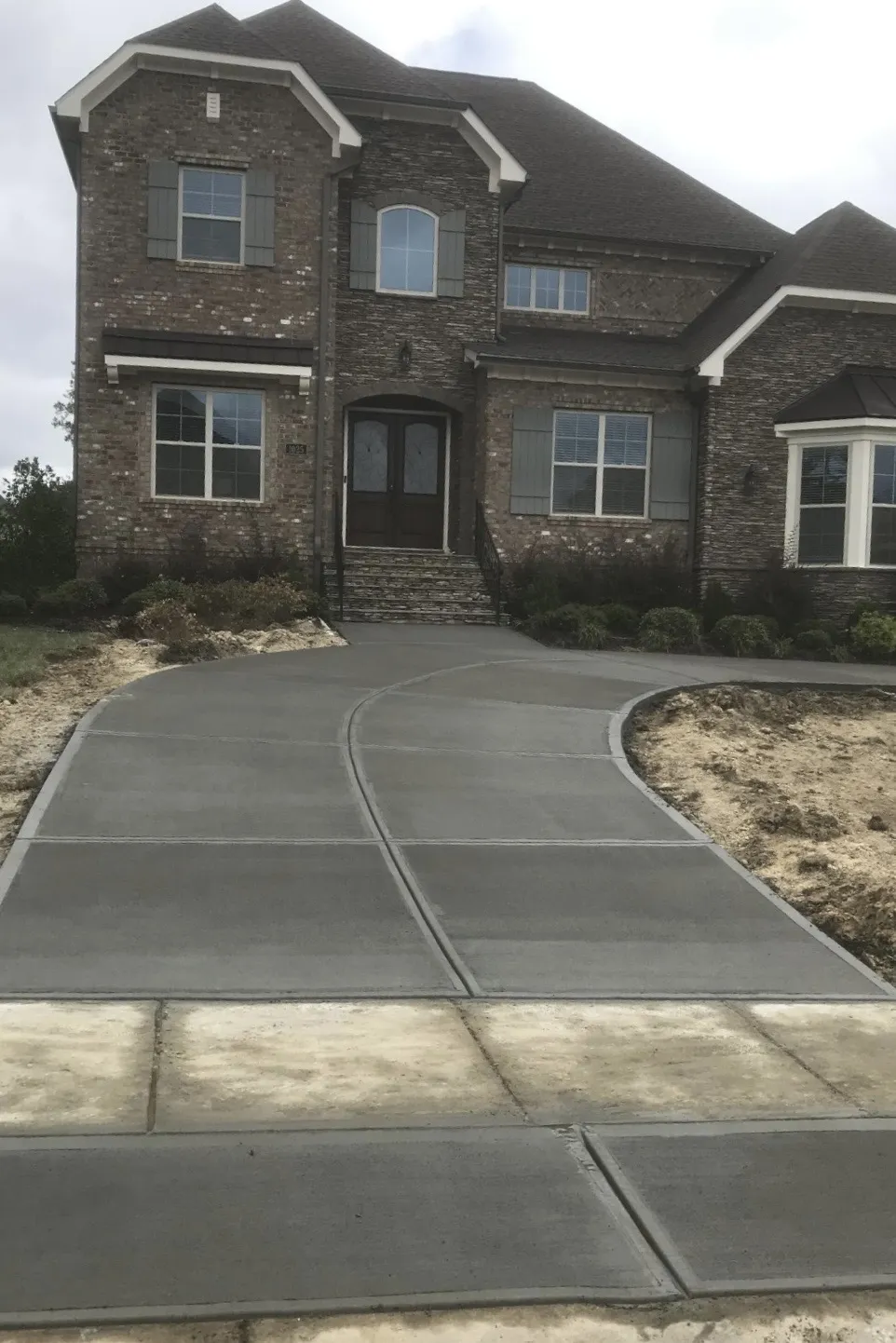 Curved concrete driveway leading to a large brick home